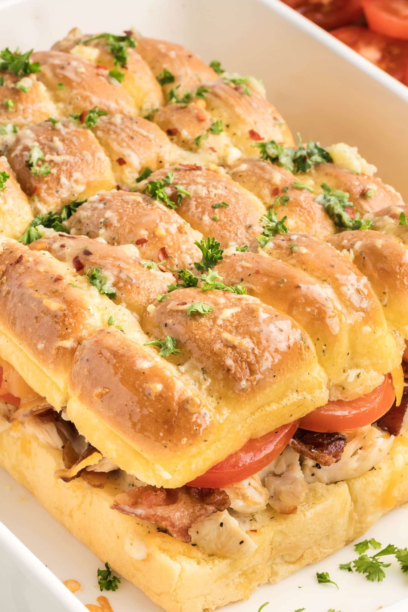 Sideview of a bacon ranch chicken sliders showing layers of melted cheese, bacon, chicken, and tomato with visible garlic butter on golden top bun. Hostess At Heart