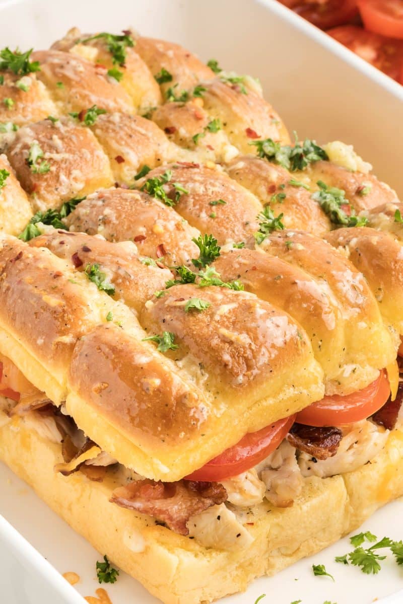 Sideview of a bacon ranch chicken sliders showing layers of melted cheese, bacon, chicken, and tomato with visible garlic butter on golden top bun. Hostess At Heart