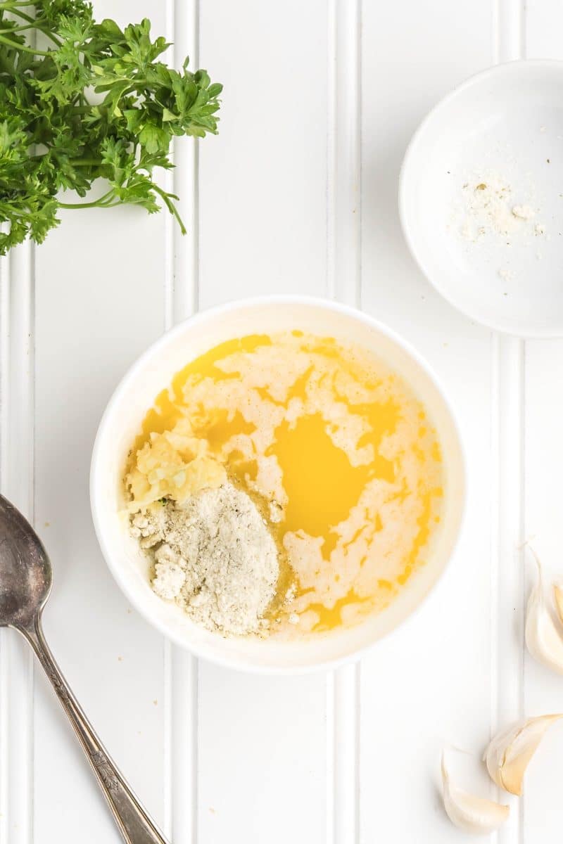 Small glass bowl containing melted garlic ranch butter mixture with visible ranch seasoning. Hostess At Heart