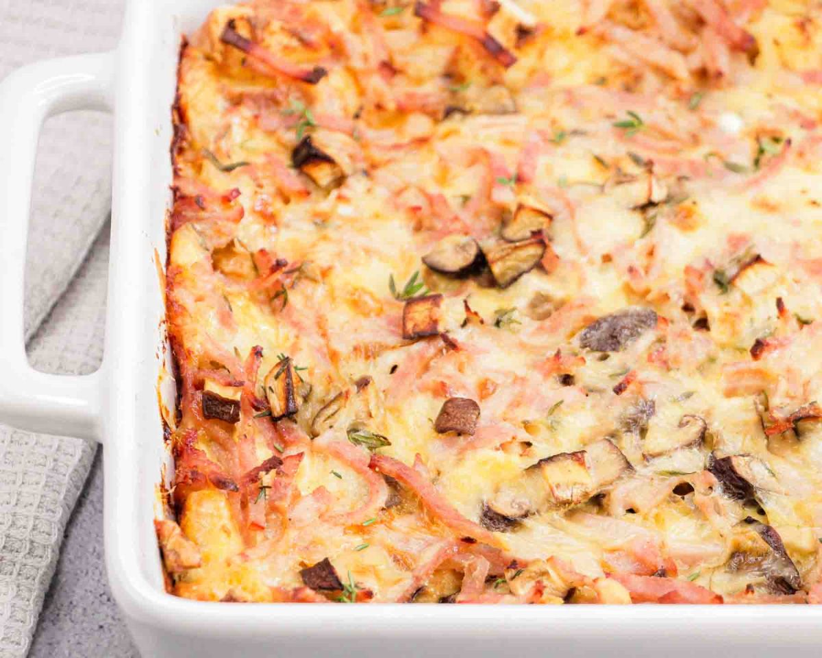 Partial view of Golden brown ham and cheese mushroom breakfast strata fresh from the oven in white baking dish. Hostess At Heart