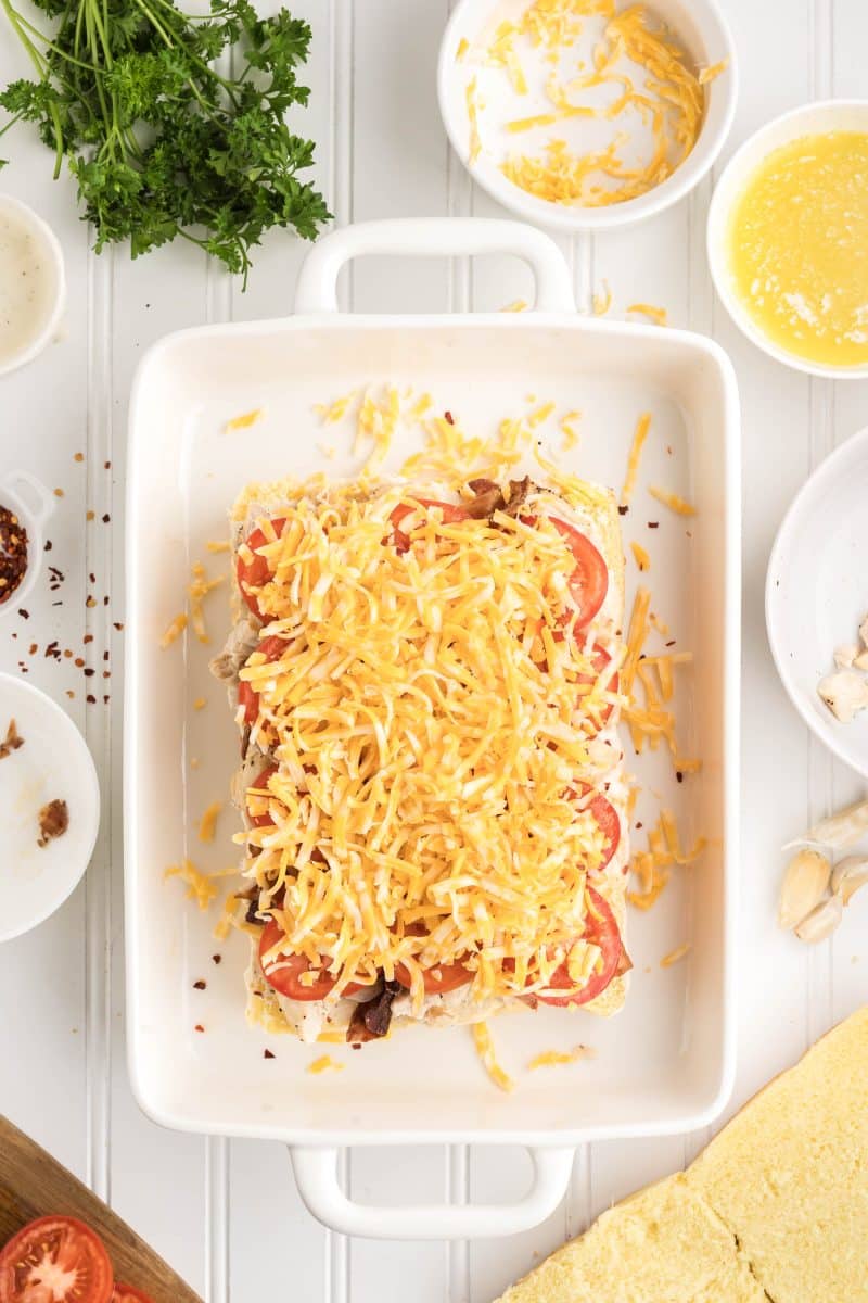 Shredded Colby-Jack cheese being sprinkled over chicken and bacon filled slider rolls before adding top buns. Hostess At Heart