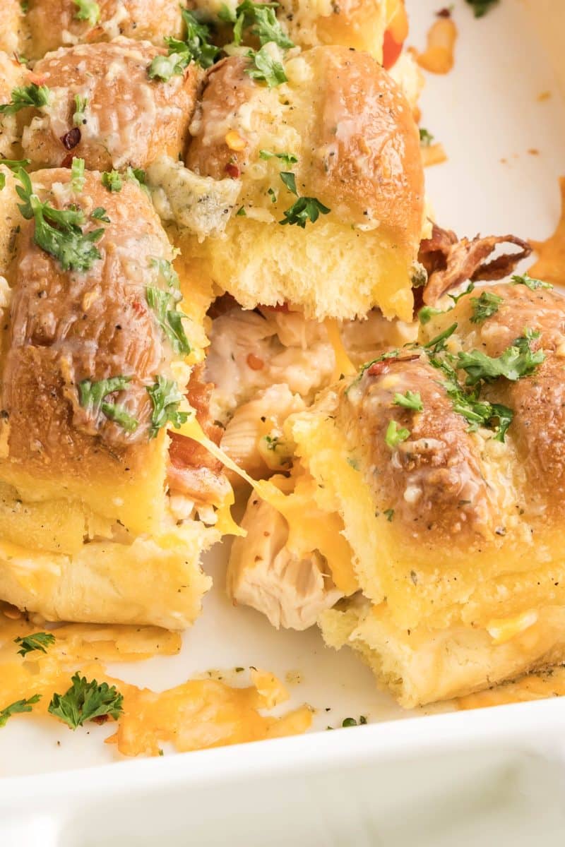Close-up of chicken bacon ranch sliders pulled apart showing melted cheese, crispy bacon, and juicy chicken filling between golden brown buns. Hostess At Heart