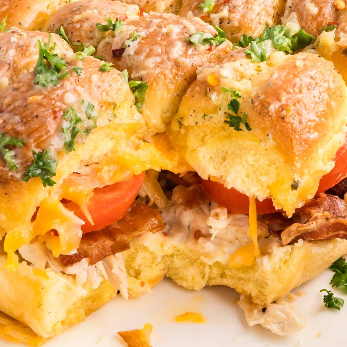 Close-up sideview of chicken bacon ranch sliders showing melted cheese, crispy bacon, and juicy chicken filling between golden brown buns. Hostess At Heart