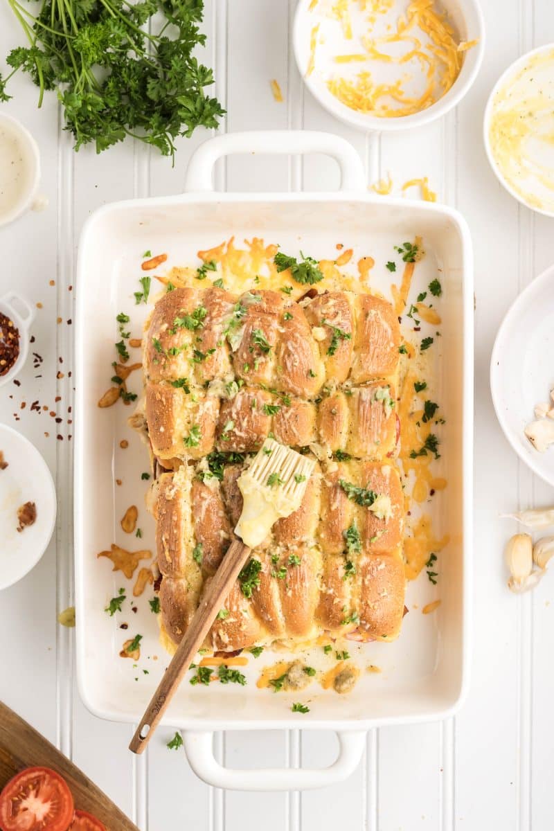 Bacon chicken ranch sliders in a white baking dish garnished with fresh parsley and with visible garlic butter on golden top bun. Hostess At Heart