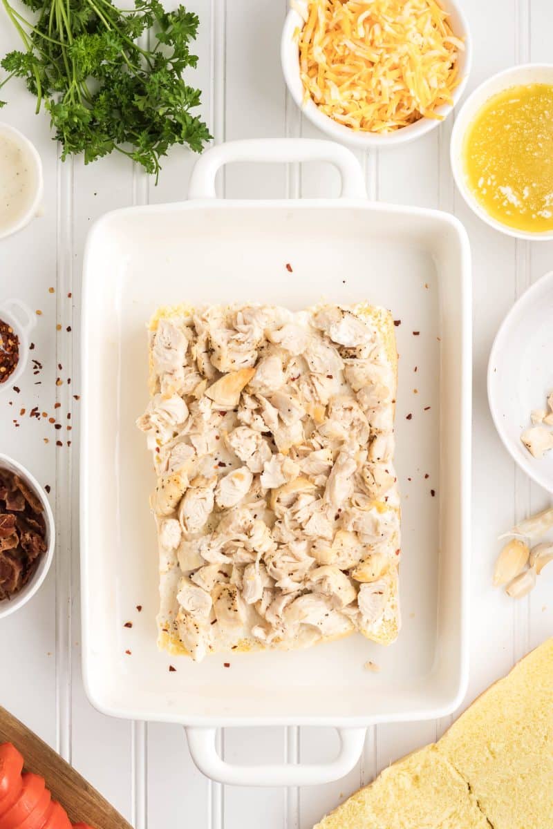 Slider rolls being assembled with a layer of chopped chicken. Hostess At Heart