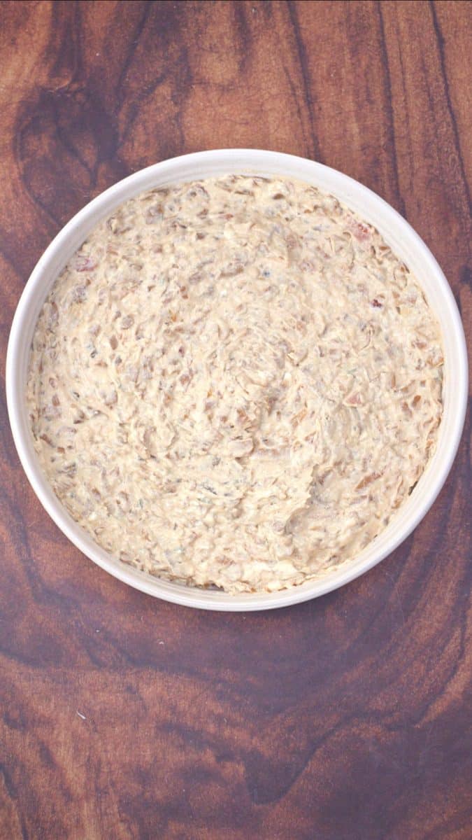 Top down view of creamy caramelized onion dip topped with crispy bacon pieces in white serving bowl. Hostess At Heart