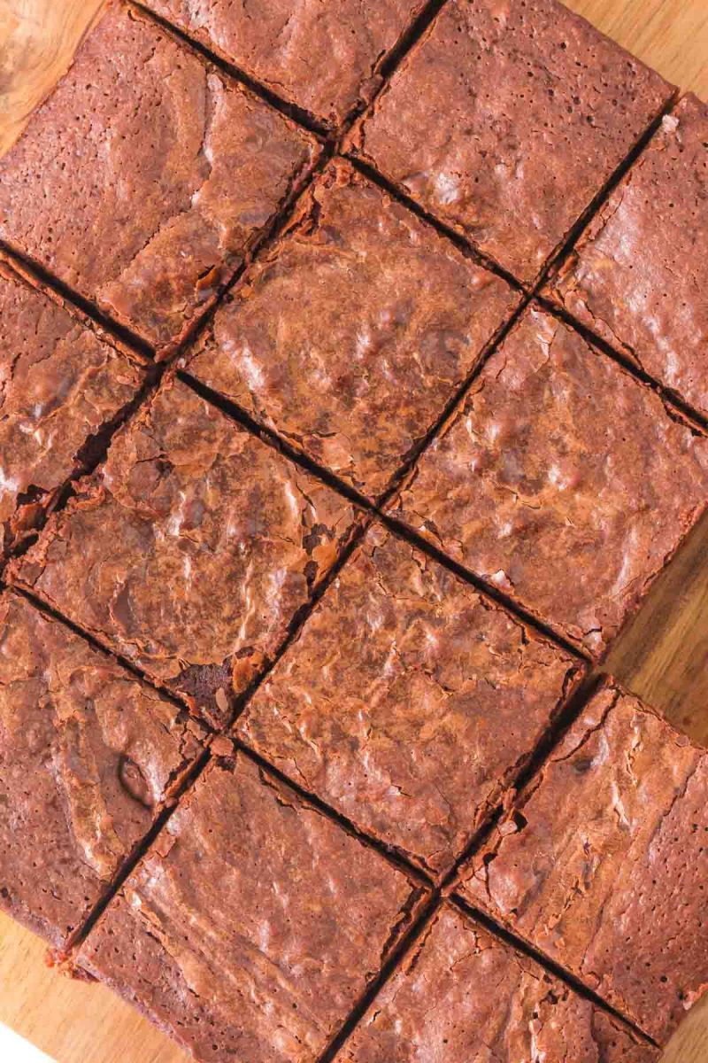 Top down view of sliced fudgy sourdough discard brownies with a crinkled top on a wooden cutting board. One piece is gone. Hostess At Heart