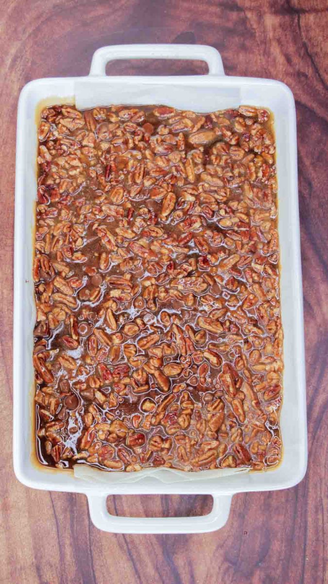 9x13 baking dish with unbaked pecan praline topping a baked brownie ready for the oven