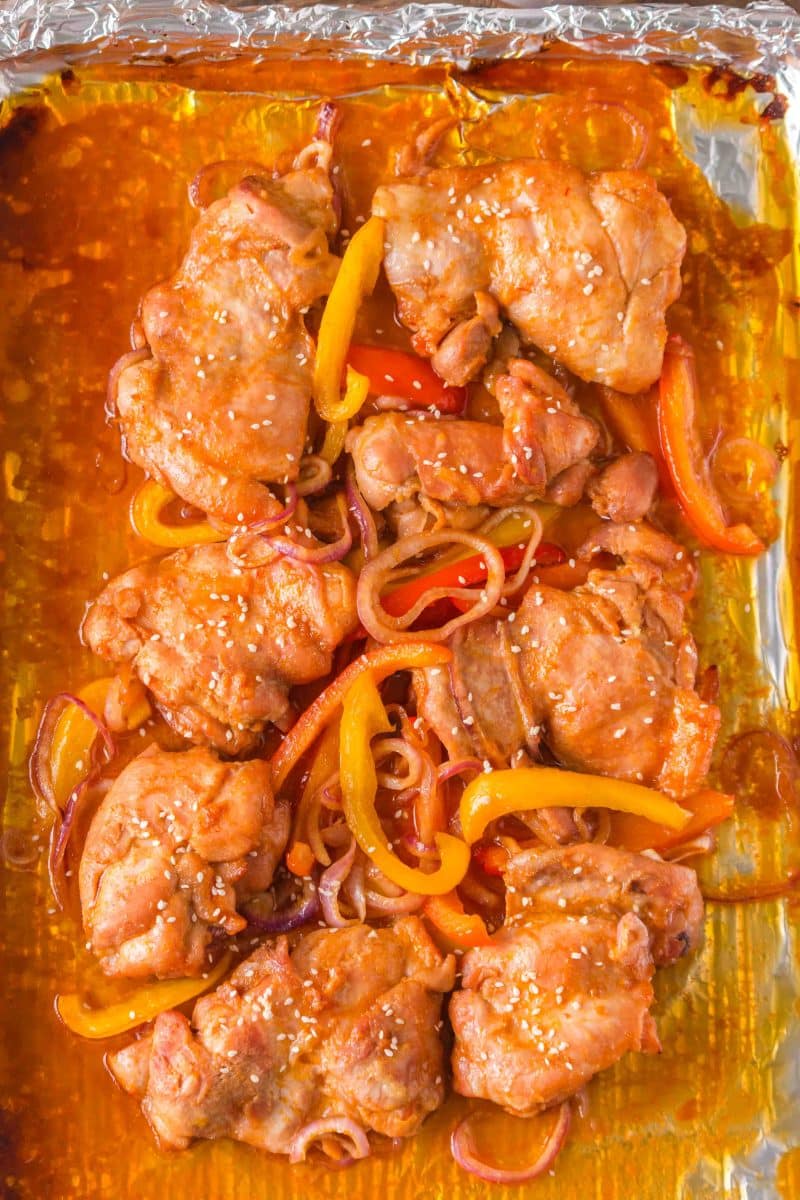 Saucy baked honey garlic chicken thighs with caramelized peppers and onions on sheet pan right out of the oven. Hostess At Heart