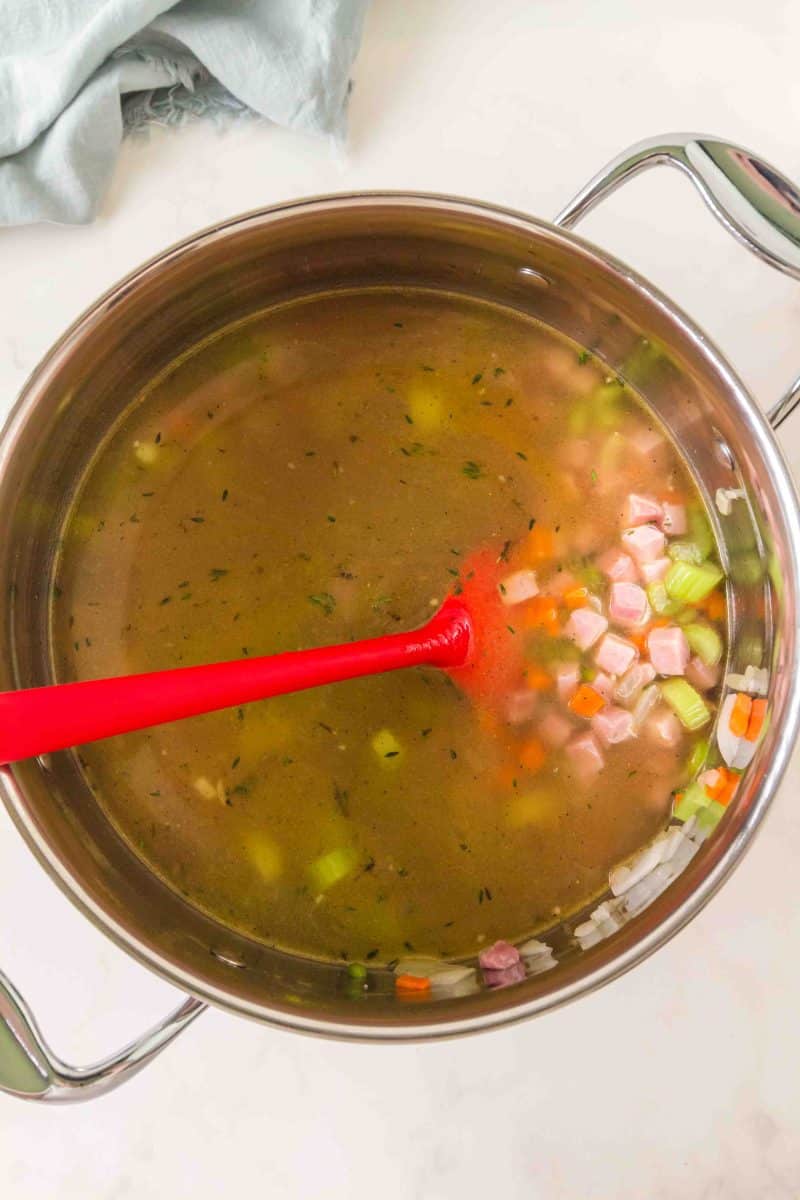 Broth added to diced carrots, celery, diced ham, and onions in a large pot to make an easy split pea soup recipe. Hostess At Heart