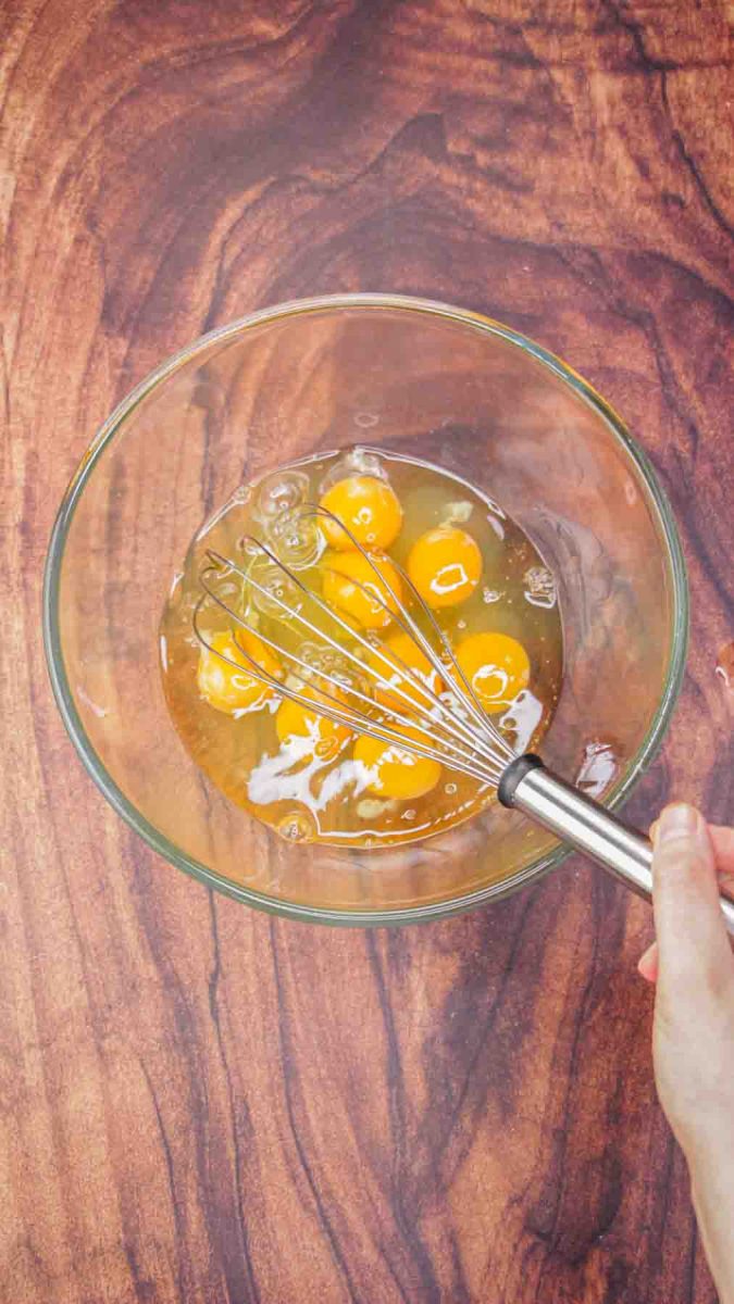 A glass mixing bowl filled with raw eggs ready to be whisked together to make a breakfast casserole. Hostess At Heart