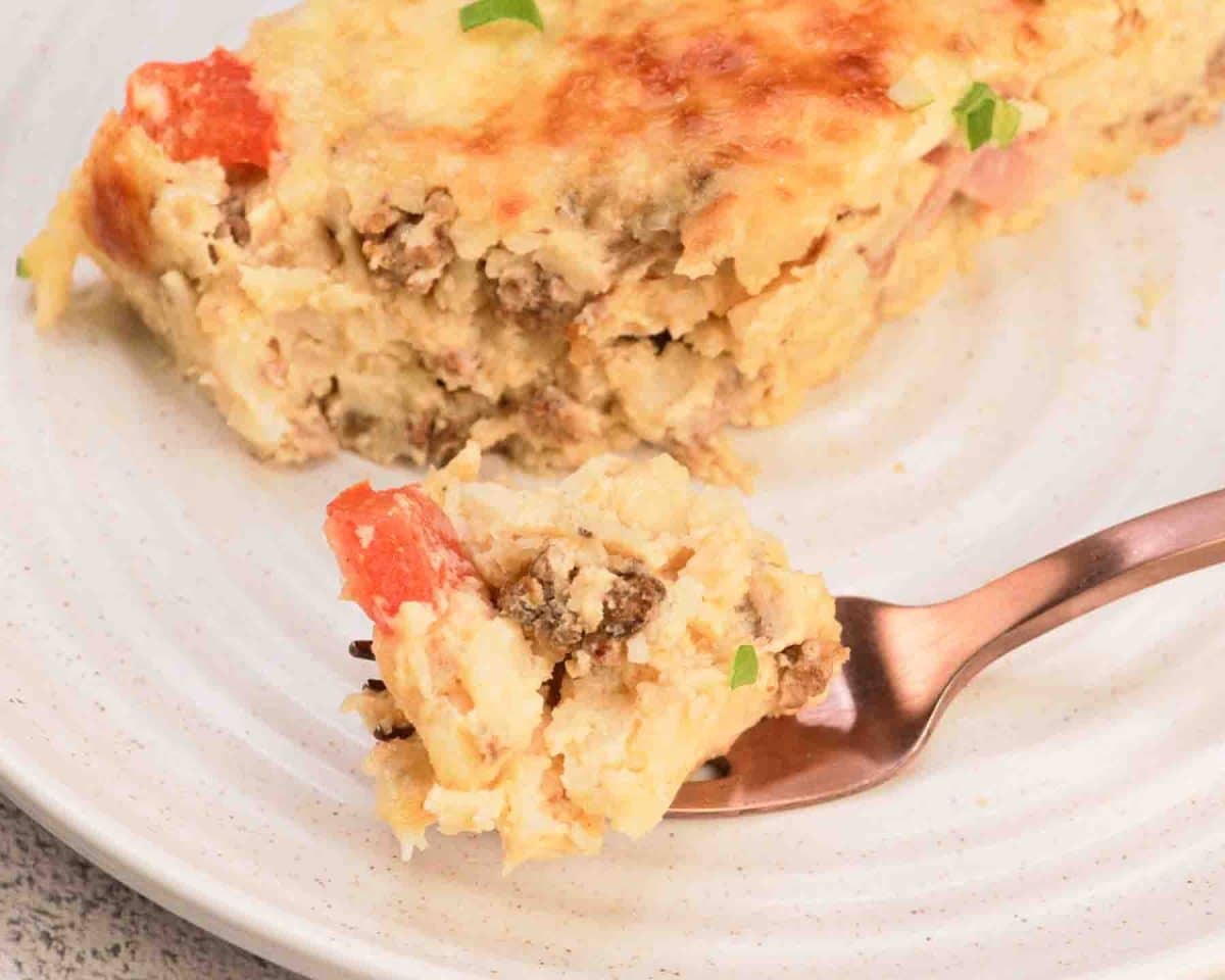 Top down view of a fork filled with a bite of Sausage, egg and Hashbrown casserole for a golden brown slice. Hostess At Heart