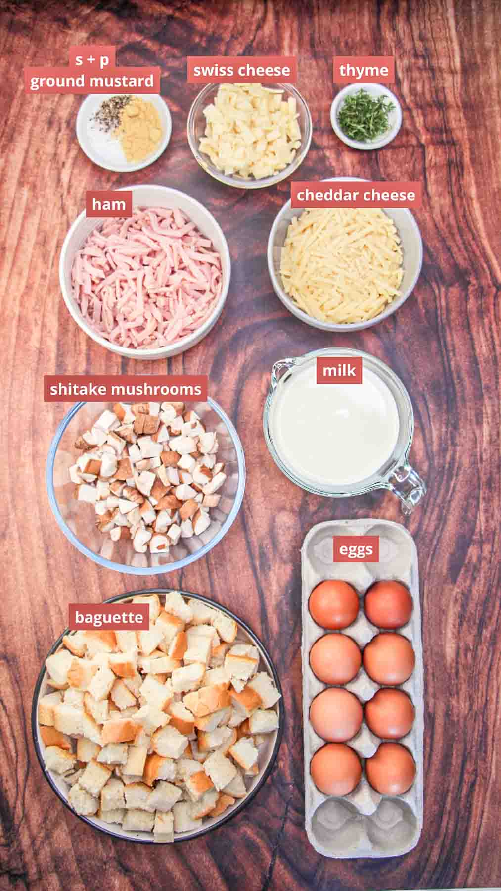 Ingredients for breakfast strata including cubed bread, ham, mushrooms, eggs, milk, and shredded cheese on kitchen counter. Hostess At Heart