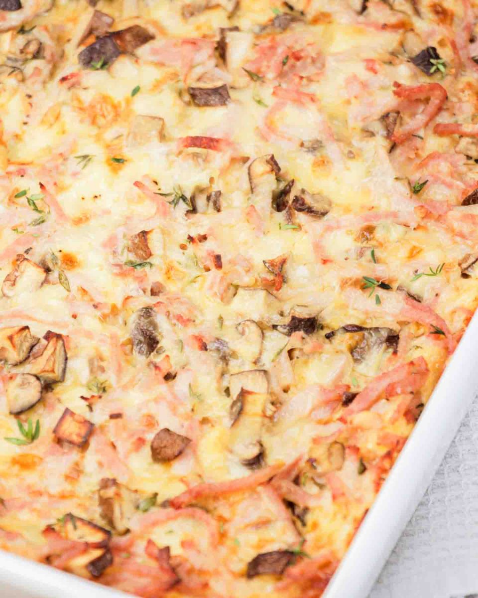 Closeup partial view of a golden brown ham and cheese breakfast strata fresh from the oven in white baking dish. Hostess At Heart
