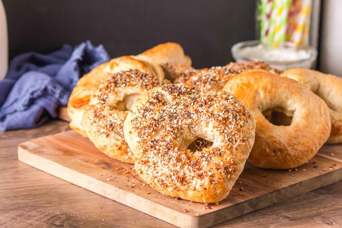Tableview of freshly baked homemade bagels recipe propped on a cutting board. Some are garnished with seasonings and some are left plain. Hostess At Heart