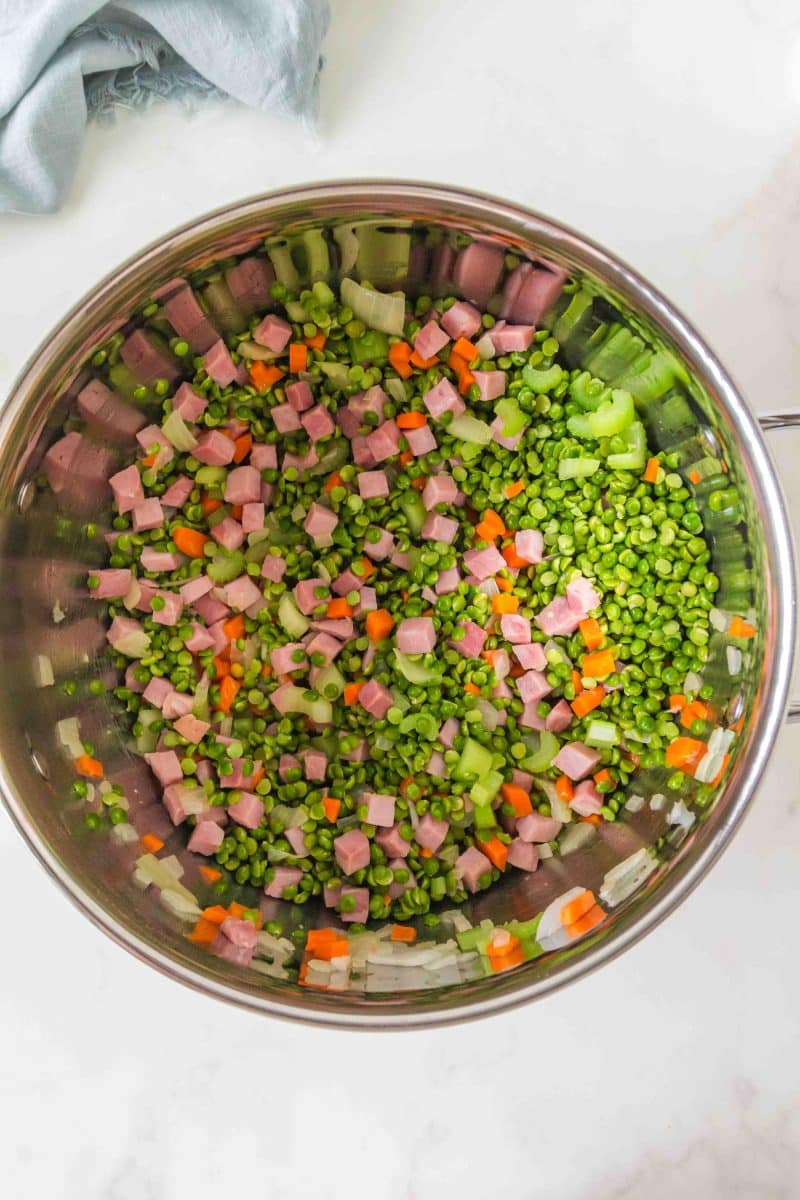 Top down view of a large pot filled with diced ham, onion, carrots, celery, and dried split peas to make leftover ham and split pea soup. Hostess At Heart