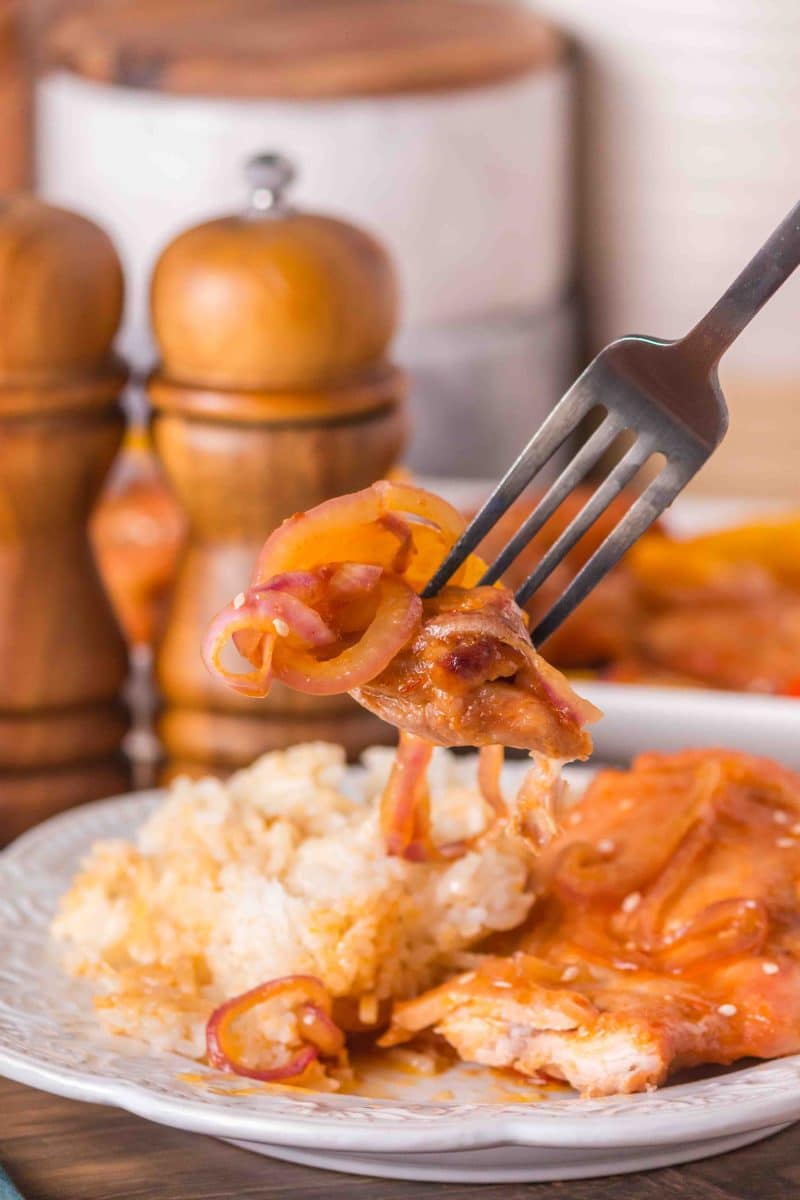 A forkful of juicy honey chicken and vegetables hovering over the dinner plate - Hostess At Heart