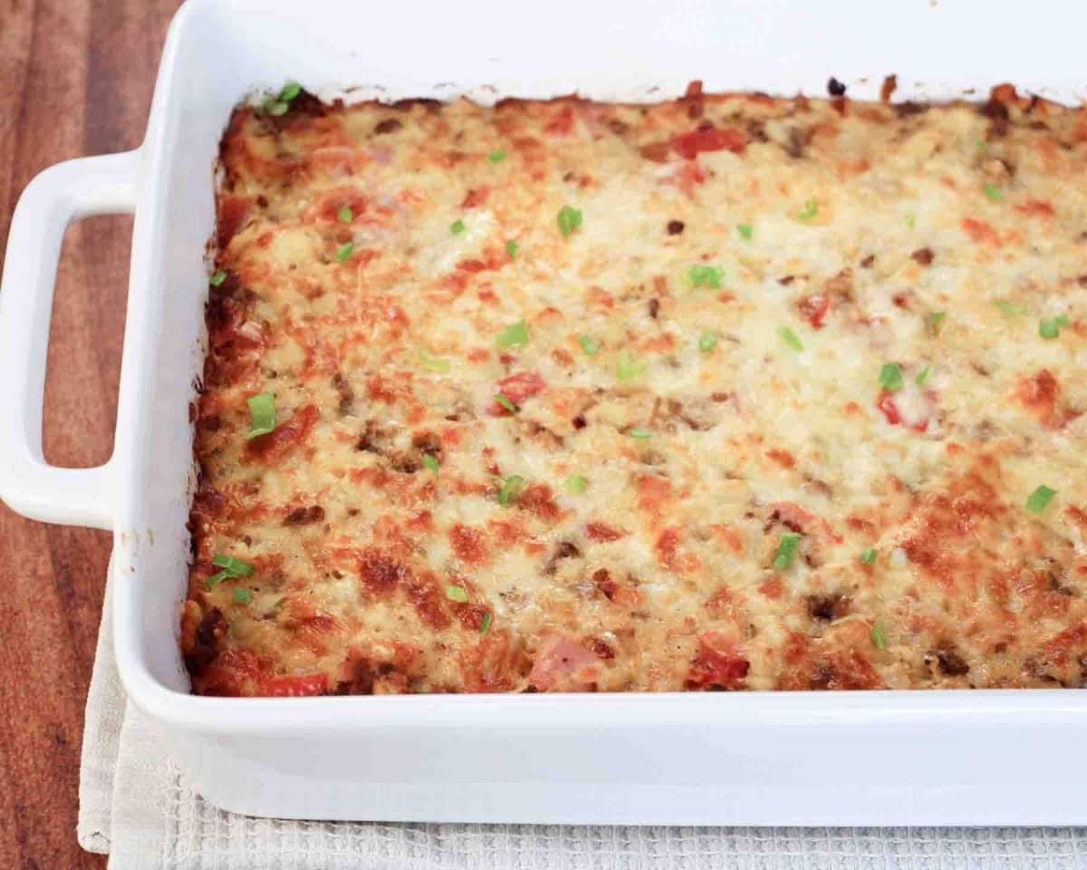 An angled table view of golden brown egg and sausage casserole with melted cheese fresh from oven - Hostess At Heart