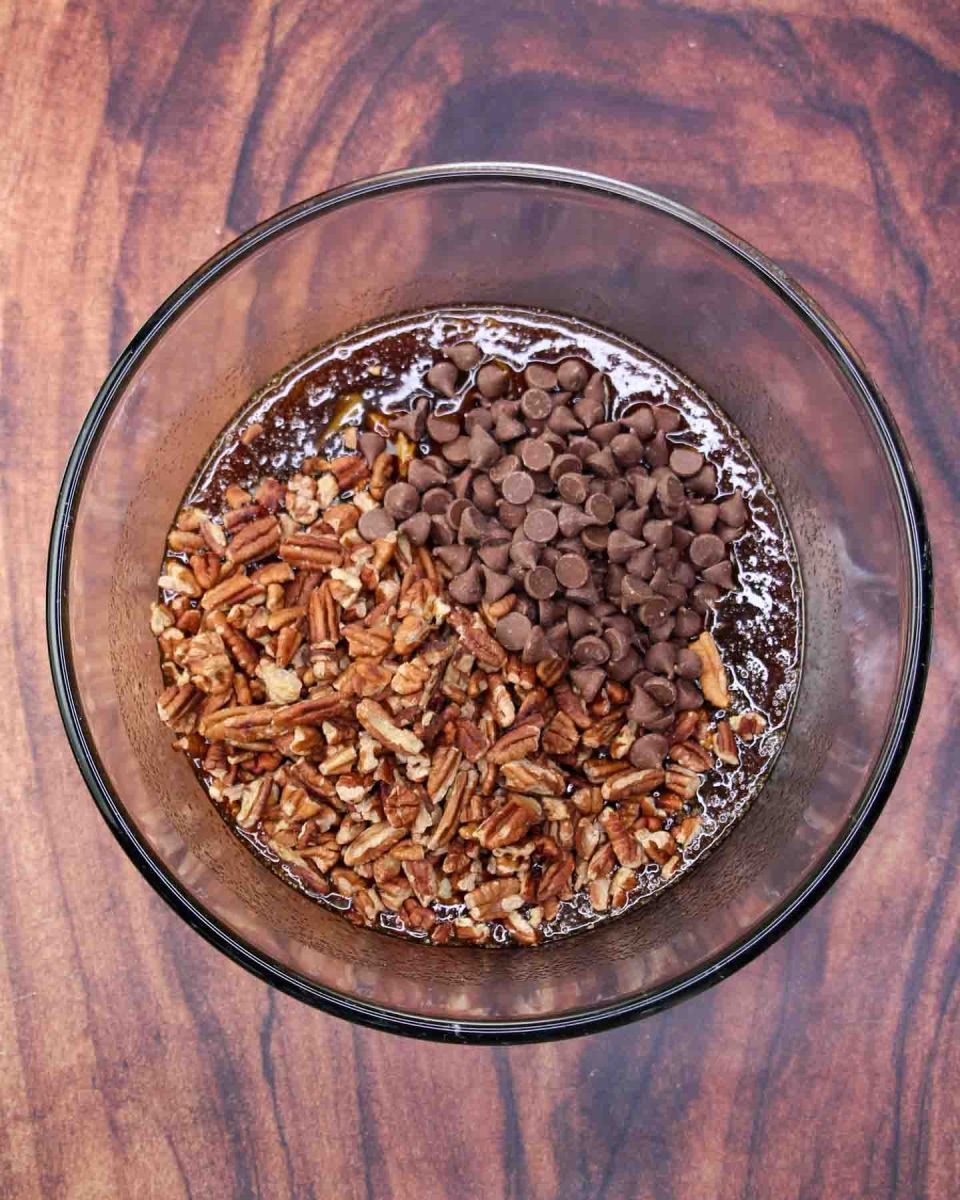 Chopped pecans and chocolate chips added to a mixing bowl filled with pecan pie ingredients; brown sugar, corn syrup, butter, eggs and bourbon - Hostess At Heart