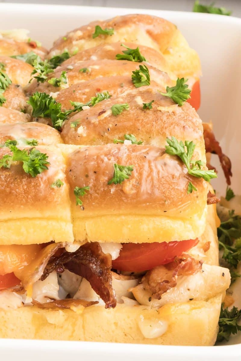 Sideview of a chicken bacon ranch slider showing layers of melted cheese, bacon, chicken, and tomato with visible garlic butter on golden top bun. Hostess At Heart