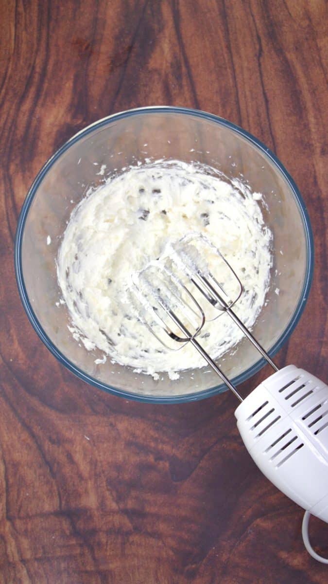 Cream cheese and sour cream in a mixing bowl being blended together with a mixer. Hostess At Heart