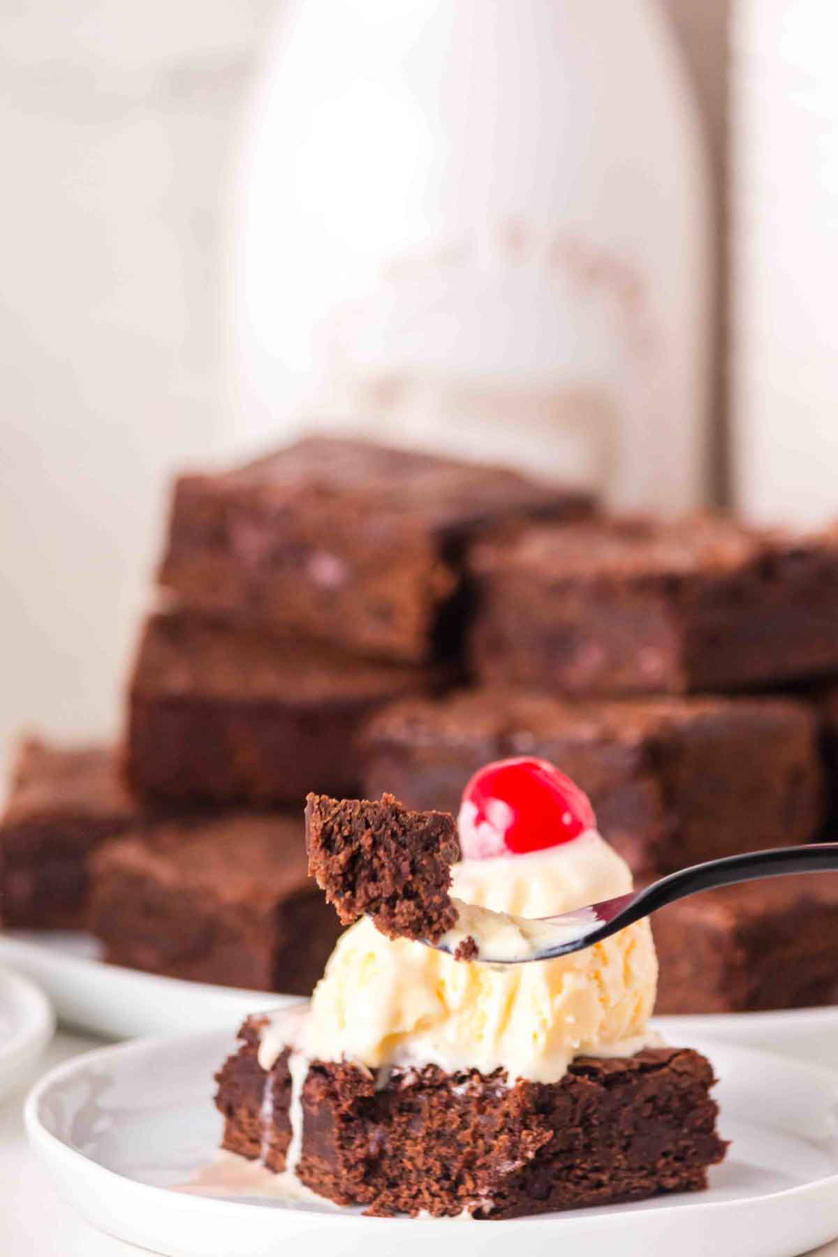 A fork filled with a bite of chocolate brownie made with sourdough starter hovering in front of the ice cream topped brownie - Hostess At Heart