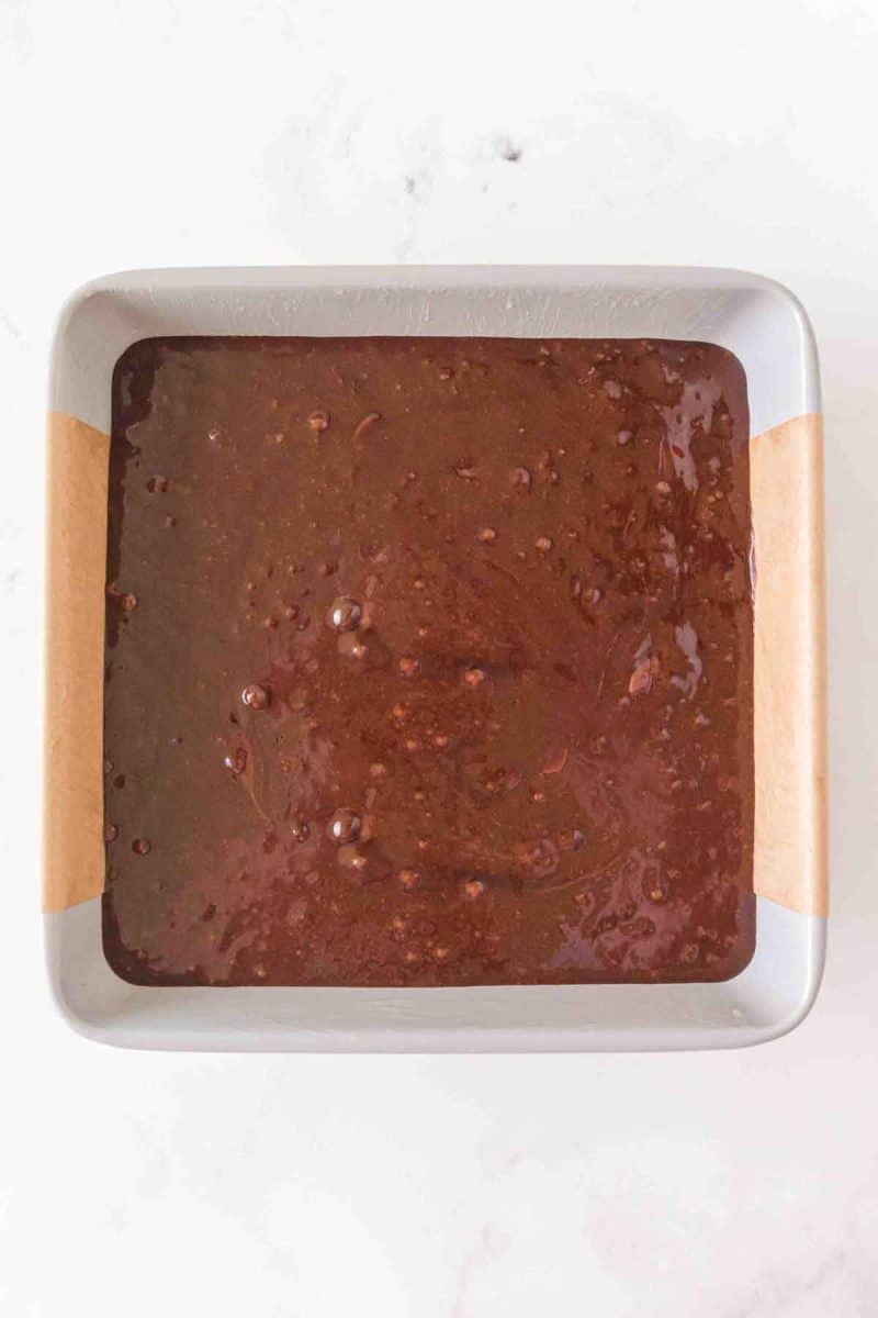 Chocolate unbaked brownie batter in a pan lined with parchment paper. Hostess At Heart