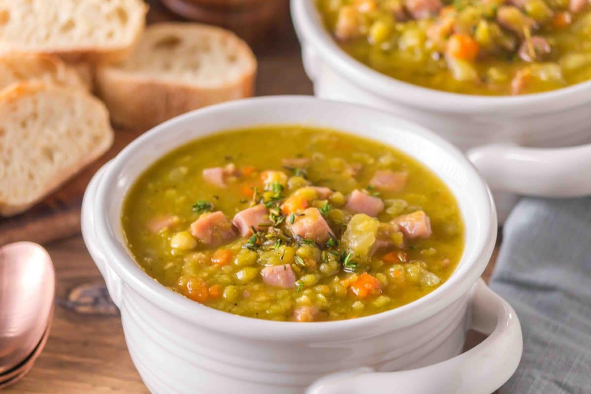 Bowl of thick, creamy split pea and ham soup with visible chunks of ham, garnished with fresh thyme. Hostess At Heart