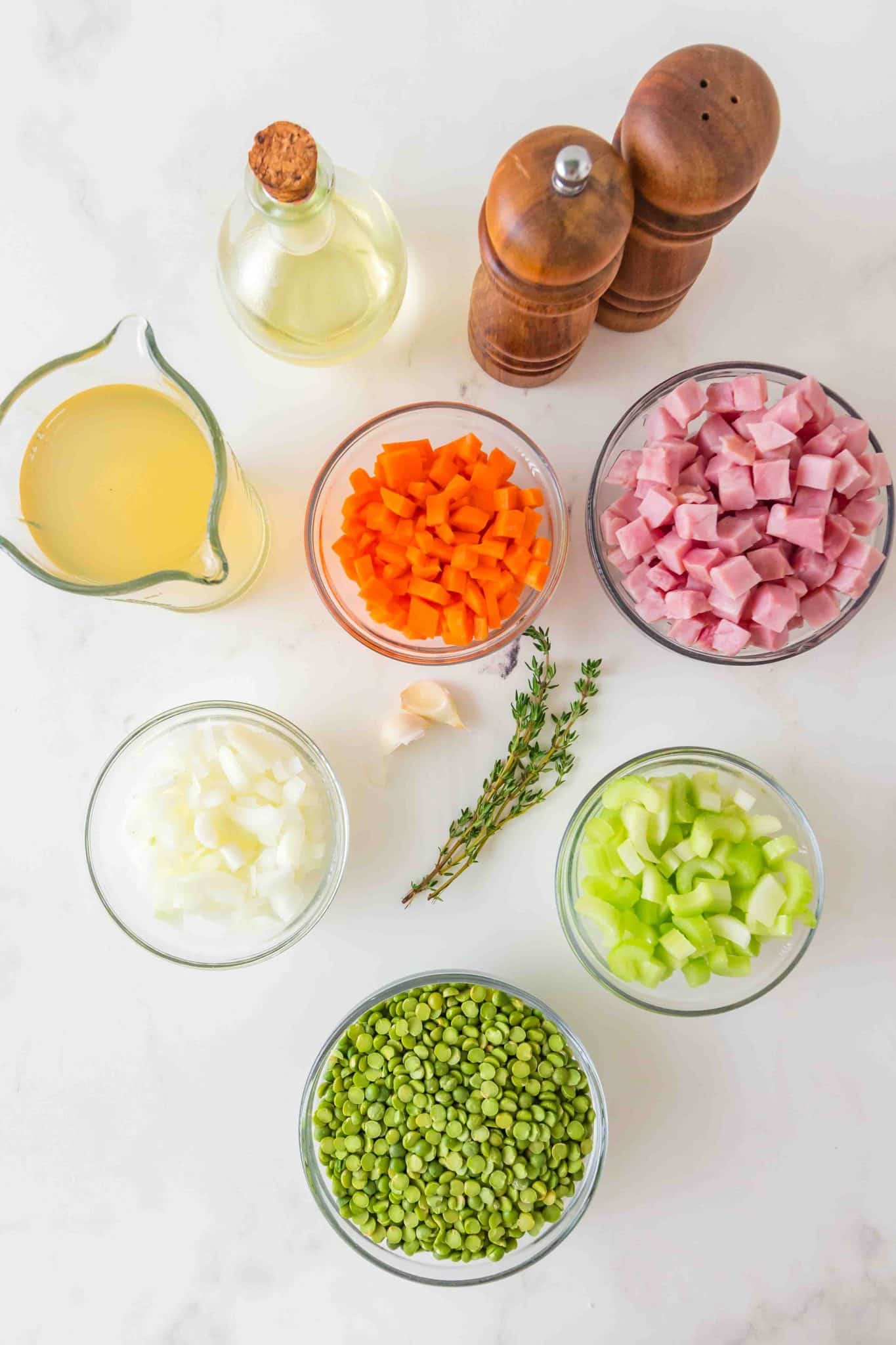 Dried green split peas, diced ham, carrots, celery, and onions arranged on a marble background for split pea and ham soup. Hostess At Heart