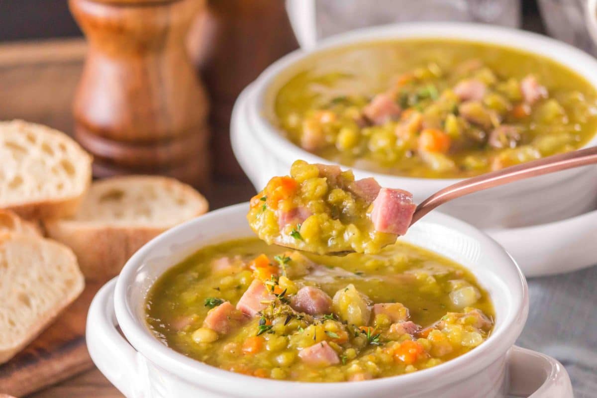 lose-up of split pea and ham soup on a spoon hovering over the bowl showing the thick, creamy consistency with a chunk of ham. Hostess At Heart