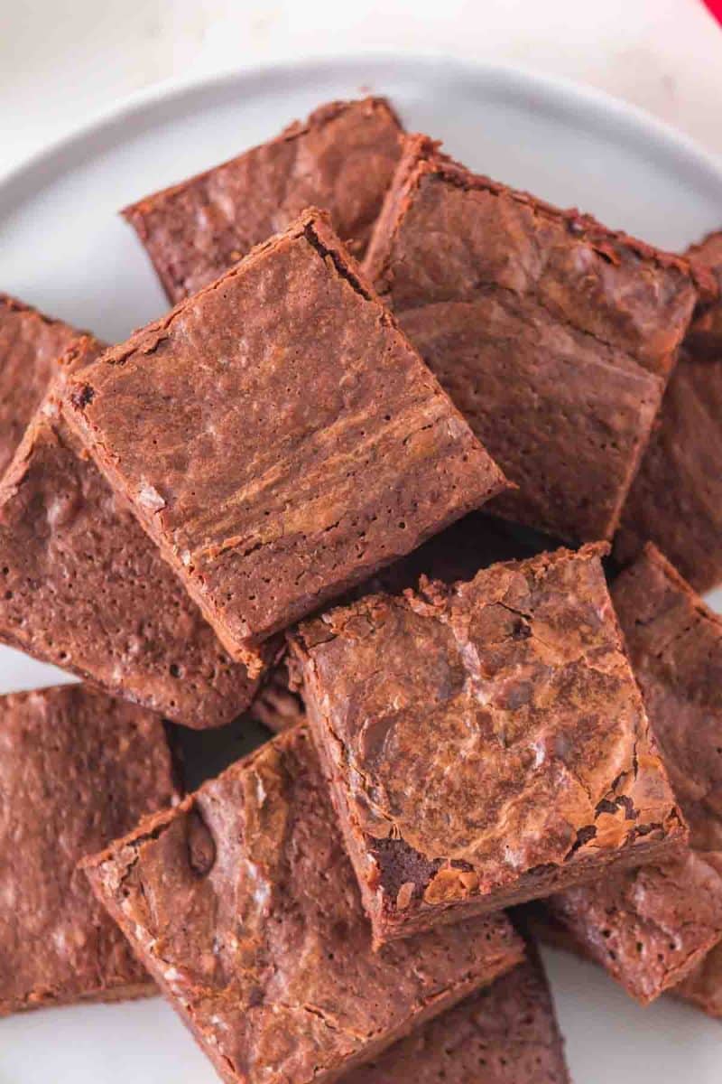 Top view of a stack of fudgy sourdough discard brownies with chocolate chips and a crinkled top on white plate. Hostess At Heart