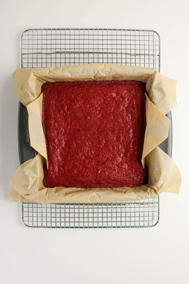 Red velvet brownie batter spread evenly in square baking pan lined with parchment paper. Hostess At Heart