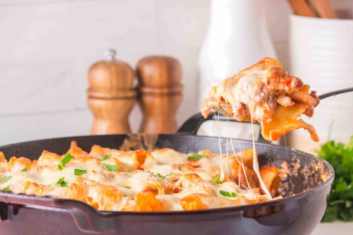 Sideview of baked rigatoni with ricotta in cast iron skillet with melted stretching from the serving spoon to the skillet. Hostess At Heart