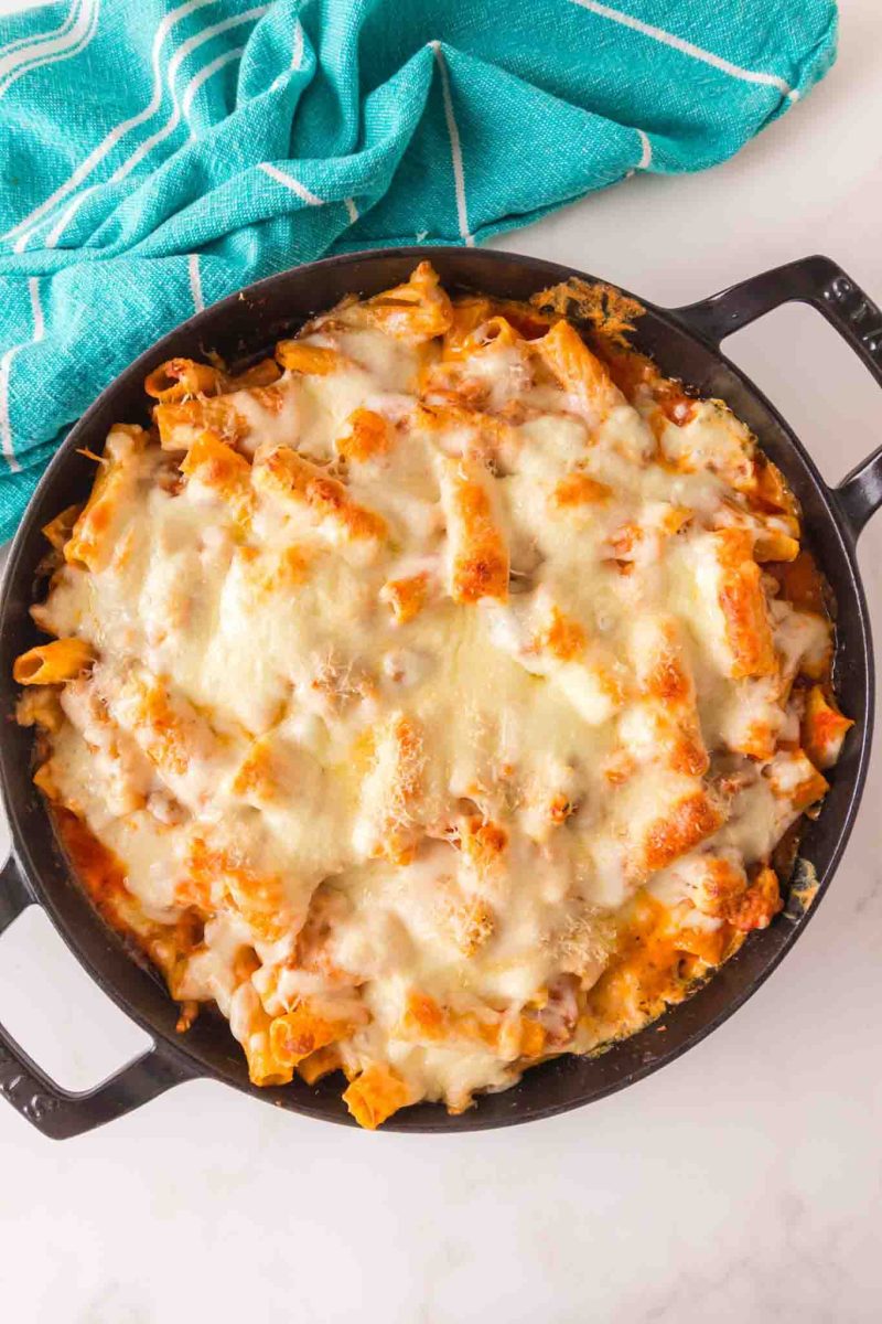 Baked rigatoni with sausage in cast iron skillet with melted cheese covering the top fresh from the oven - Hostess At Heart