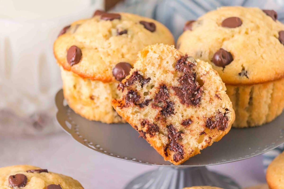 A sourdough chocolate chip muffin cut in half showing melted chocolate chips propped against whole sourdough muffins. Hostess At Heart