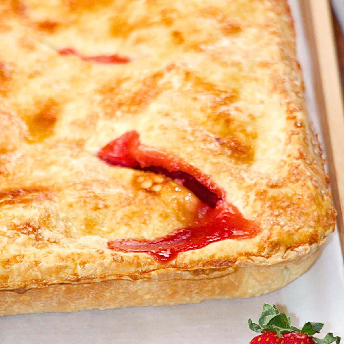 Angled view of a golden brown square strawberry pie with filling oozing out of the vented crust - Hostess At Heart