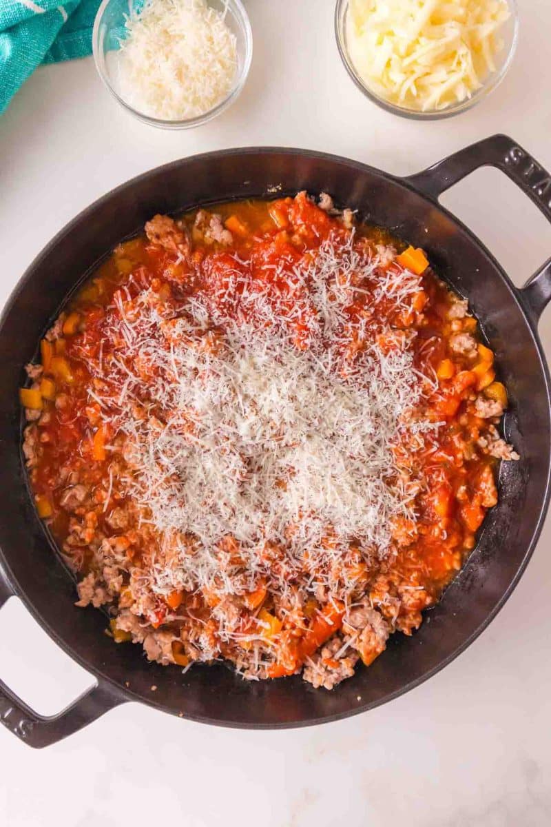 Sprinkled parmesan cheese on top of a cast-iron skillet of rigatoni ready for the oven - Hostess At Heart