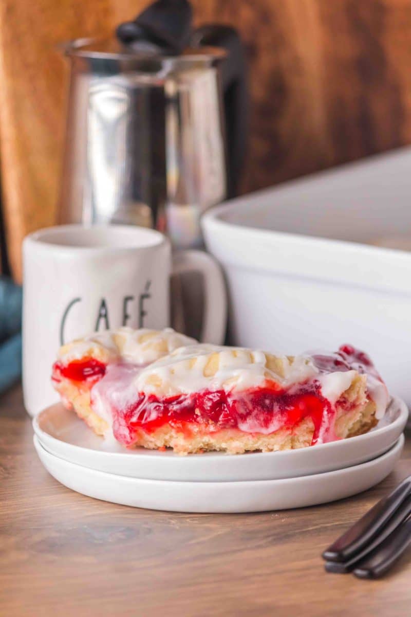 Cherry Pie Bars with vanilla glaze drizzled on top, spooned on a white plate. Hostess At Heart
