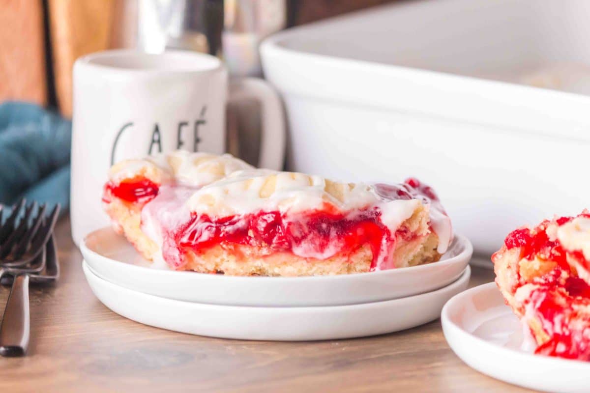 Sideview of Easy Cherry Pie Bars showing layers of crust, cherry filling, and crumb topping on a white plate. Hostess At Heart