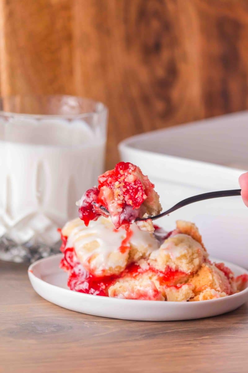 A fork filled with a bite of easy Cherry Pie Bars showing layers of crust, cherry filling, and crumb topping. Hostess At Heart