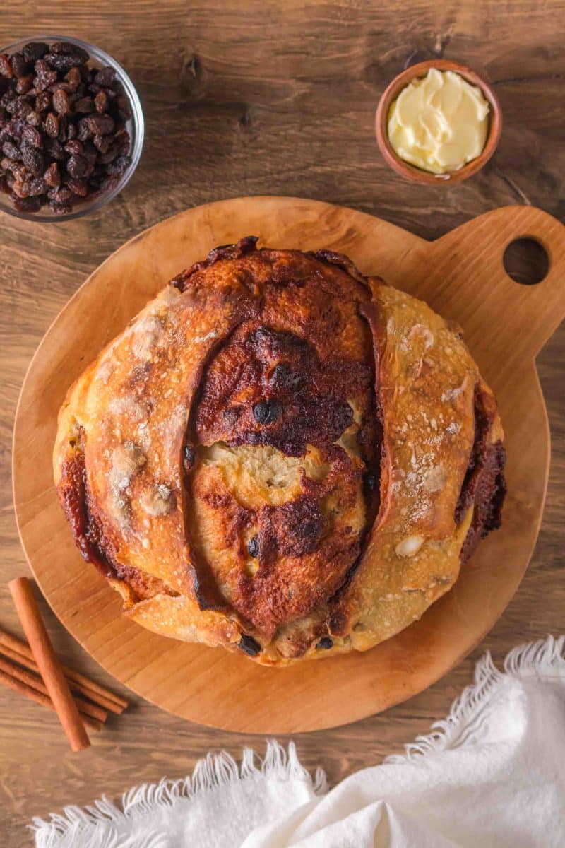 Golden brown sourdough cinnamon raisin bread with visible raisins sitting on a cutting board. Hostess At Heart