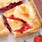 A corner slice of a strawberry slab pie pulled away from the square dessert showing a thick strawberry filling oozing out of a butter crust. Hostess At Heart