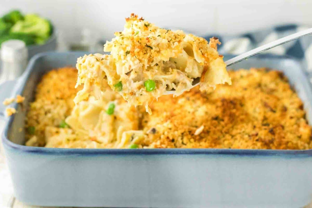 A large spoon holding a serving of tuna and noodles hovering over the baking dish. Hostess At Heart