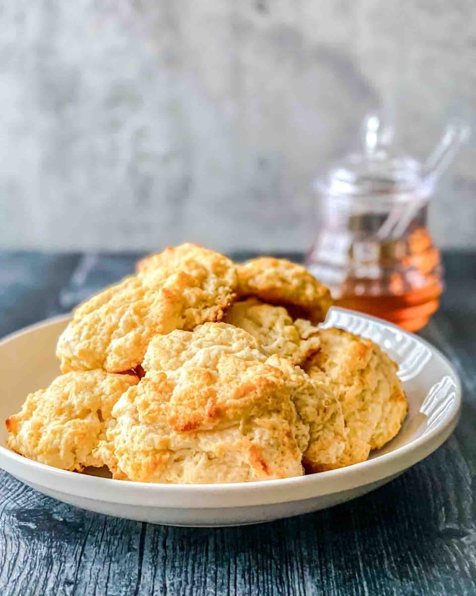 Angled view of a serving dish on a table filled with holden brown honey buttermilk drop biscuits. Hostess At Heart