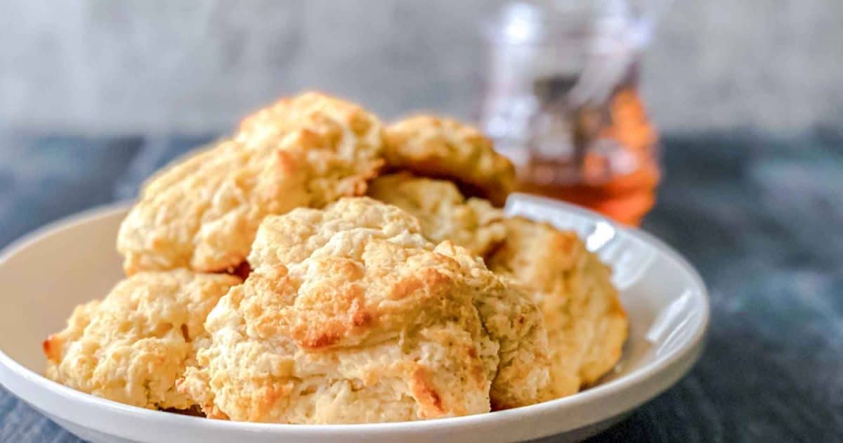 Sideview of a serving dish filled with honey butter biscuit recipe on the dinner table - Hostess At Heart