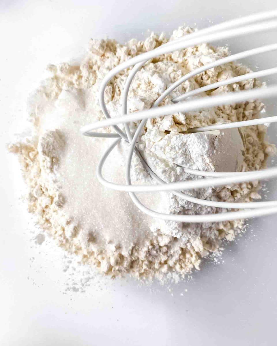 A whisk combining the dry ingredients necessary to make a honey butter biscuit recipe - Hostess At Heart