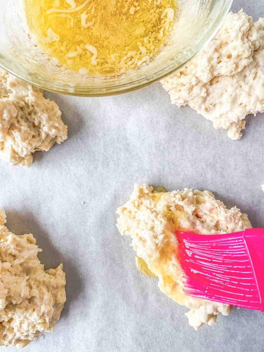 A pastry brush applying honey butter glaze to an unbaked drop biscuit. Hostess At Heart