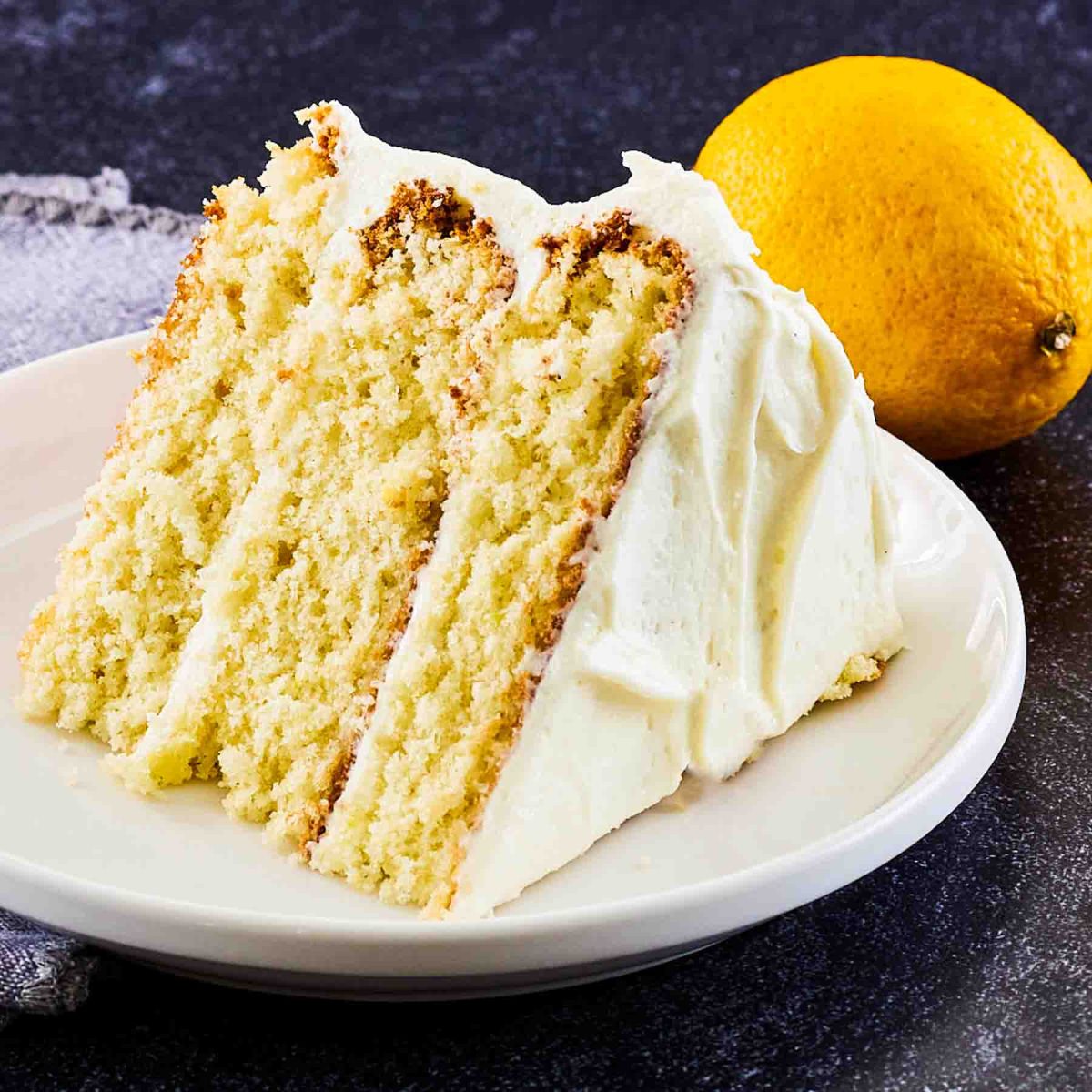 Slice of moist lemon cake with lemon cream cheese frosting on white plate showing moist yellow layers - Hostess At Heart