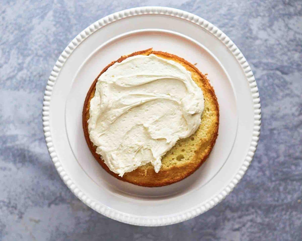 Spreading lemon cream cheese frosting over the top of lemon cake - Hostess At Heart