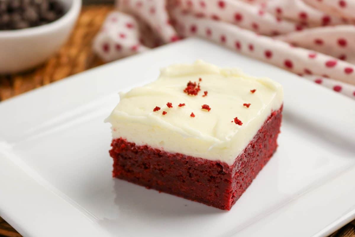 Red velvet brownie on plate with fork showing fudgy interior and cream cheese frosting layer. Hostess At Heart